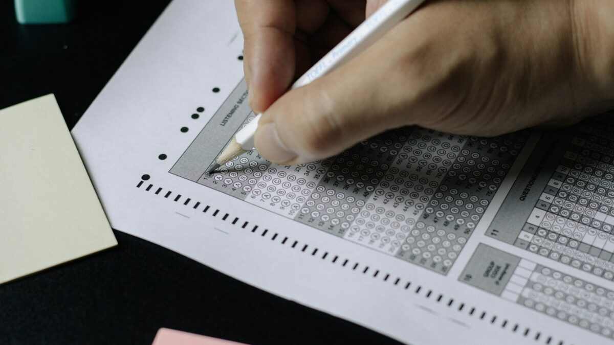 A person filling in answers on a multiple-choice test sheet with a pencil.