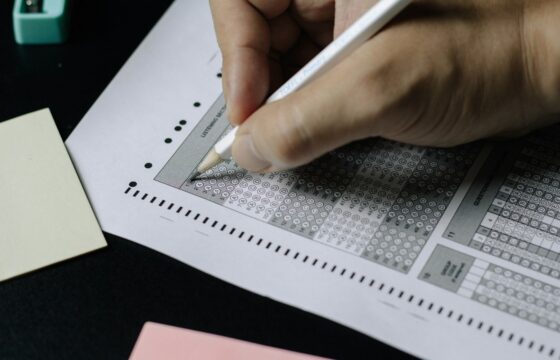 A person filling in answers on a multiple-choice test sheet with a pencil.