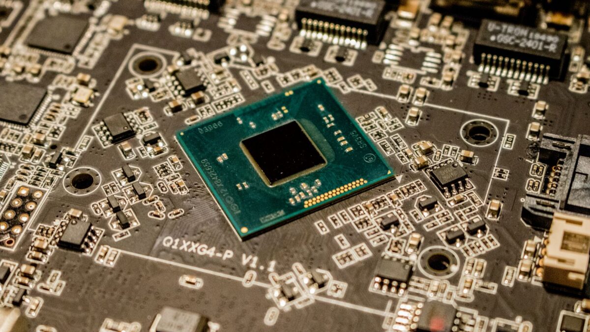 Close-up of a black microchip and electronic components on a green circuit board.