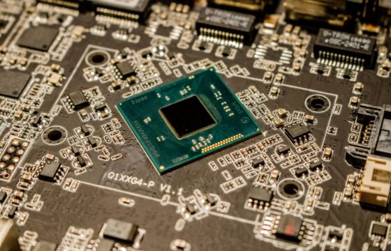 Close-up of a black microchip and electronic components on a green circuit board.